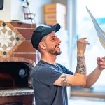 Pizzaiolo beim Schleudern des Teiges (Stendere la pizza a mano). Durch die Rotation in der Luft zieht sich der Teig quasi selbst gleichmäßig rund.