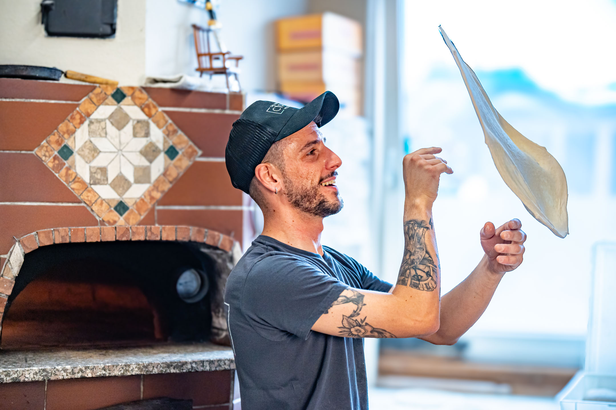 Pizzaiolo beim Schleudern des Teiges (Stendere la pizza a mano). Durch die Rotation in der Luft zieht sich der Teig quasi selbst gleichmäßig rund.
