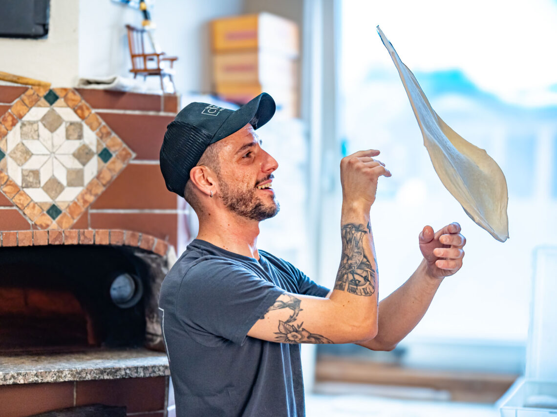 Pizzeria Ciro – Teigschleudern von Hand durch den Pizzaiolo Pizzaiolo beim Schleudern des Teiges (Stendere la pizza a mano). Durch die Rotation in der Luft zieht sich der Teig quasi selbst gleichmäßig rund.